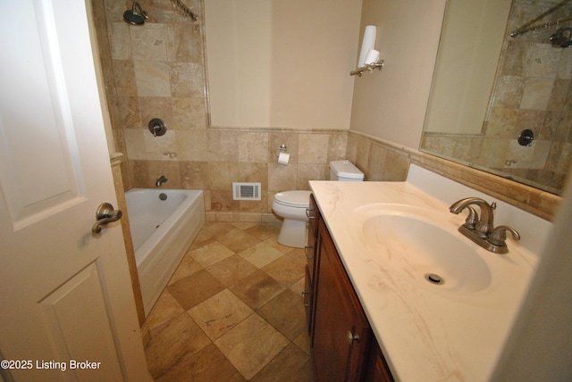 bathroom with toilet, vanity, visible vents, tile walls, and wainscoting