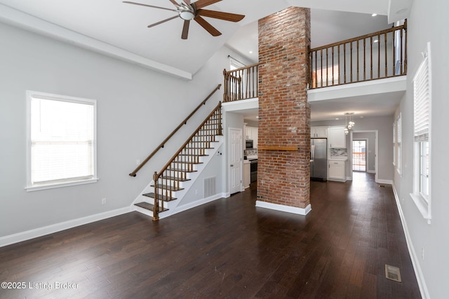 unfurnished living room featuring baseboards, visible vents, a towering ceiling, dark wood-style flooring, and stairs