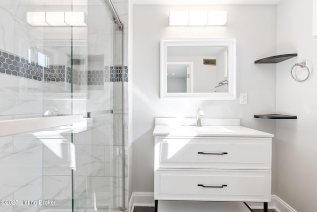 full bath featuring a marble finish shower, vanity, and baseboards