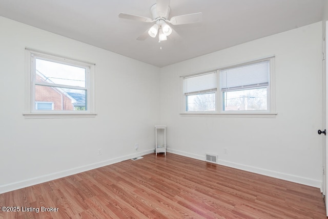 empty room featuring baseboards, light wood-style flooring, visible vents, and a wealth of natural light