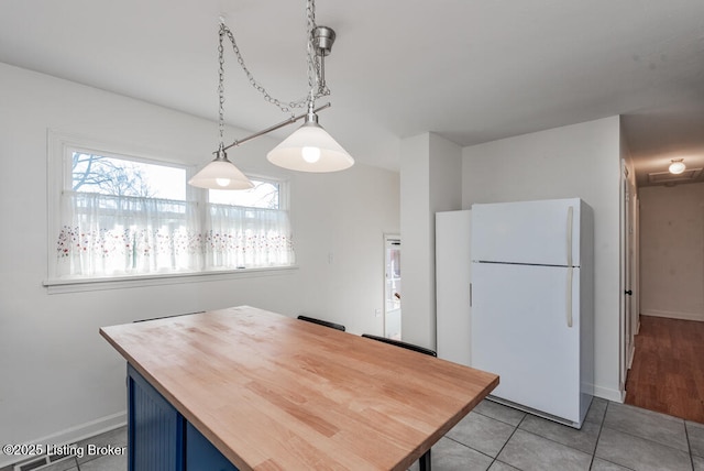 kitchen with light tile patterned floors, butcher block countertops, blue cabinetry, freestanding refrigerator, and pendant lighting