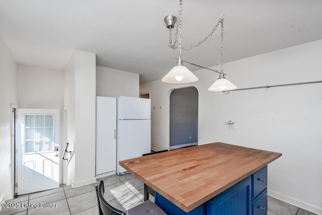 kitchen with arched walkways, butcher block countertops, freestanding refrigerator, blue cabinets, and light tile patterned flooring