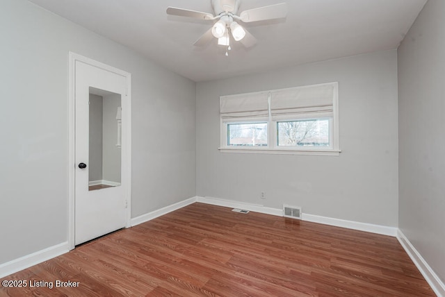 empty room with a ceiling fan, wood finished floors, visible vents, and baseboards