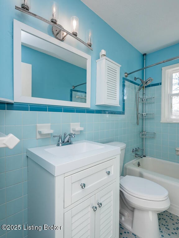 bathroom with toilet, vanity, tile walls,  shower combination, and tile patterned floors