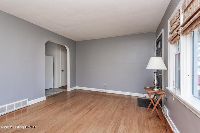 spare room with baseboards, visible vents, arched walkways, wood finished floors, and a healthy amount of sunlight