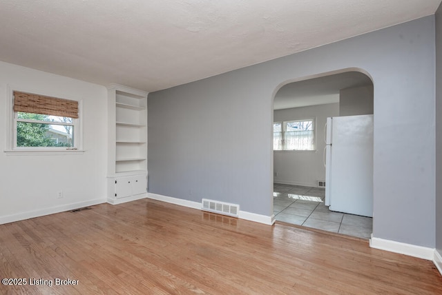 empty room featuring baseboards, visible vents, arched walkways, and wood finished floors