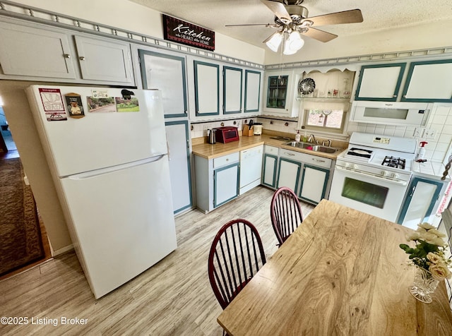 kitchen featuring light wood-style floors, white appliances, a sink, and a textured ceiling