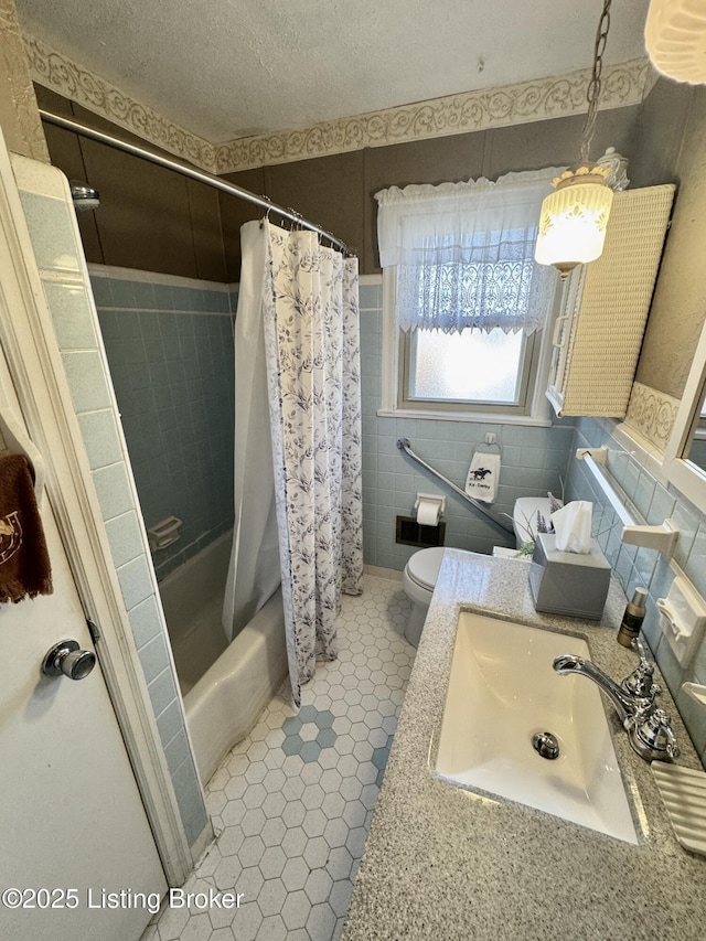 bathroom with a textured ceiling, tile patterned flooring, toilet, tile walls, and shower / bath combo with shower curtain