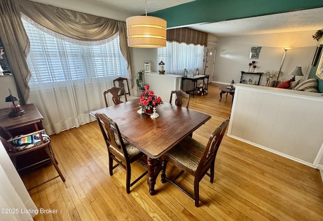 dining space with a textured ceiling, light wood-style flooring, and baseboards