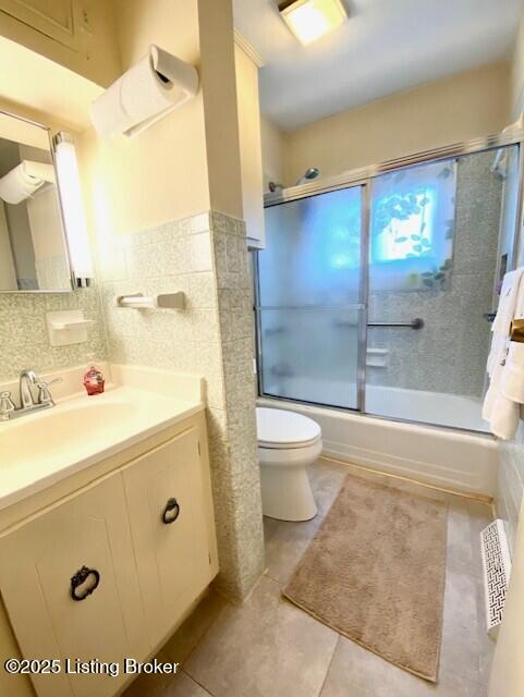 bathroom featuring tile walls, visible vents, toilet, combined bath / shower with glass door, and vanity