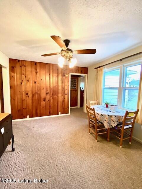 dining room with baseboards, a ceiling fan, a textured ceiling, carpet floors, and wood walls