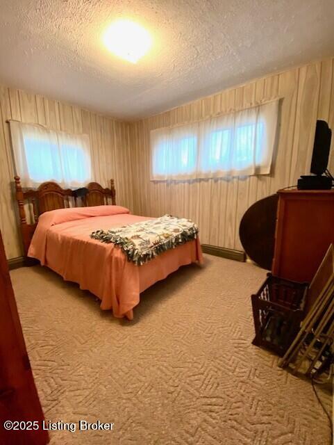 bedroom featuring wooden walls, carpet, and a textured ceiling