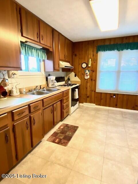 kitchen with under cabinet range hood, white range with gas stovetop, a sink, light countertops, and brown cabinets