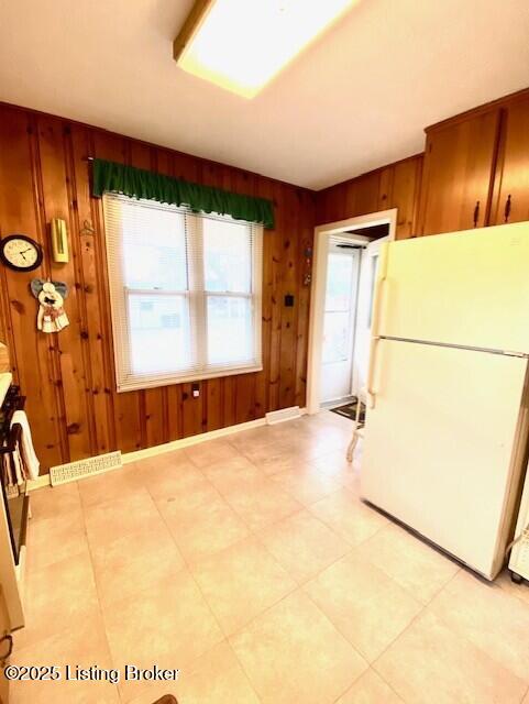 kitchen with baseboards, wooden walls, visible vents, and freestanding refrigerator