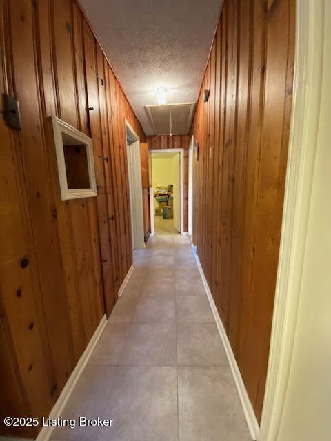 hallway featuring a textured ceiling, wood walls, attic access, and baseboards