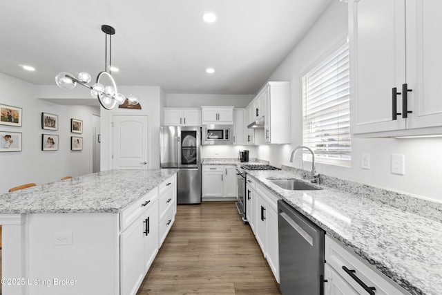 kitchen featuring a kitchen island, wood finished floors, stainless steel appliances, white cabinetry, and a sink