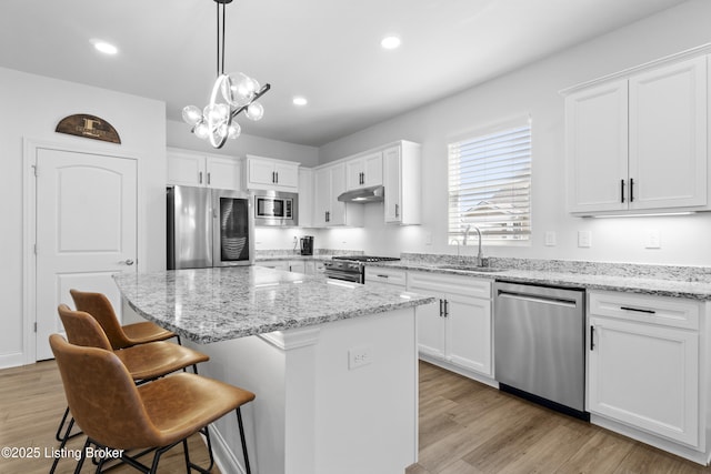 kitchen with under cabinet range hood, a sink, white cabinetry, appliances with stainless steel finishes, and a kitchen bar