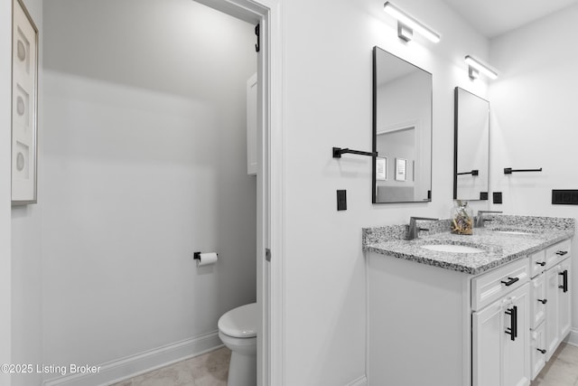 bathroom with toilet, double vanity, baseboards, and a sink