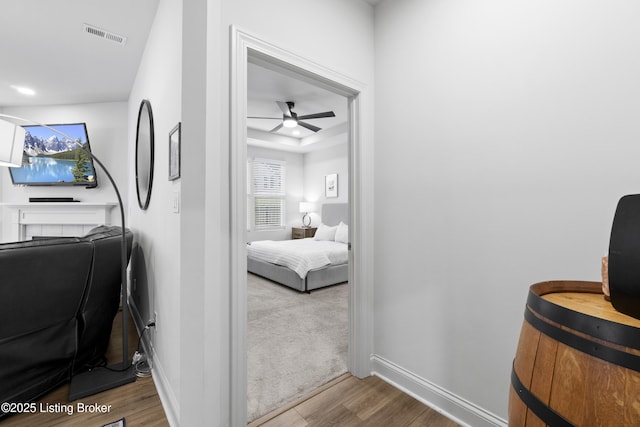 home office featuring wood finished floors, a ceiling fan, visible vents, baseboards, and a raised ceiling