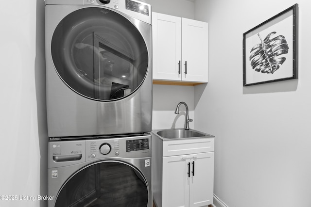 laundry room with stacked washer and clothes dryer, cabinet space, a sink, and baseboards