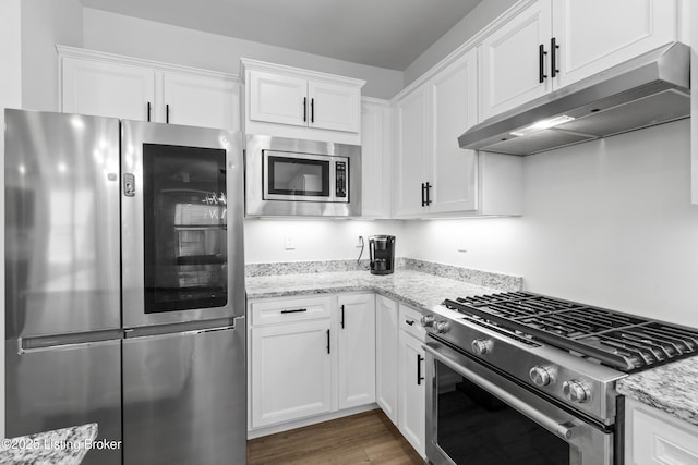 kitchen with appliances with stainless steel finishes, white cabinets, under cabinet range hood, and wood finished floors