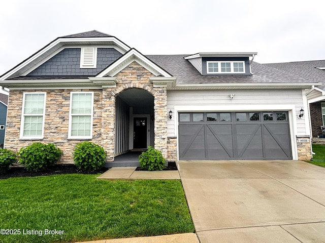 craftsman-style home featuring a front yard, an attached garage, driveway, and stone siding