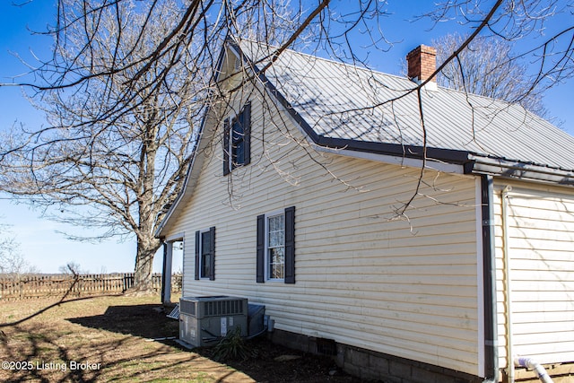 view of side of property featuring a chimney, fence, metal roof, and central AC