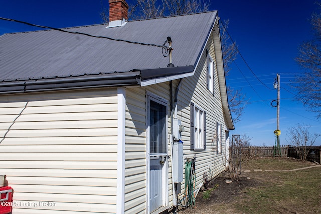 view of side of property with metal roof, a chimney, and fence