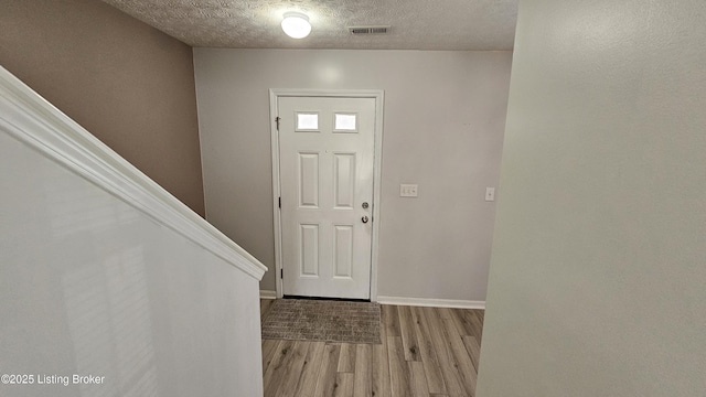 entrance foyer featuring baseboards, visible vents, stairs, a textured ceiling, and light wood-type flooring