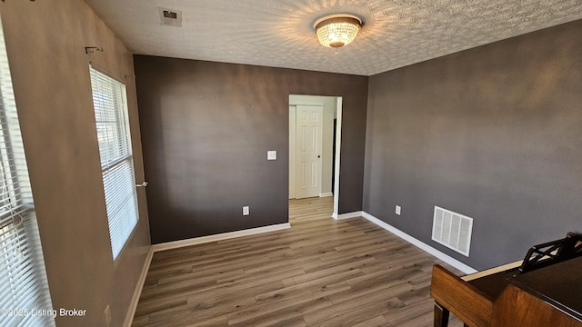 unfurnished room with a textured ceiling, wood finished floors, visible vents, and baseboards