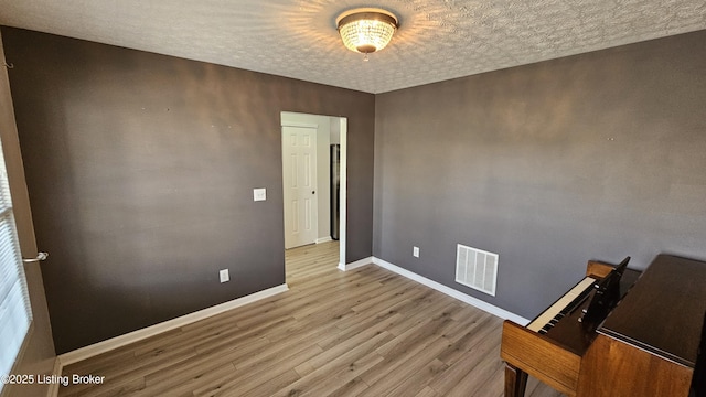 empty room featuring a textured ceiling, wood finished floors, visible vents, and baseboards