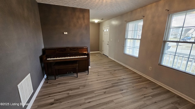 living area with a textured ceiling, visible vents, a wealth of natural light, and wood finished floors