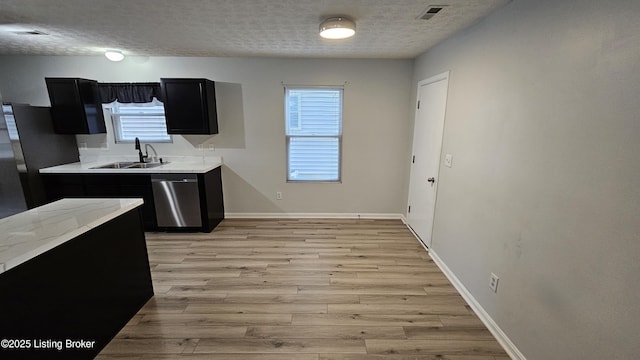 kitchen with dark cabinets, a sink, visible vents, light wood-style floors, and dishwasher