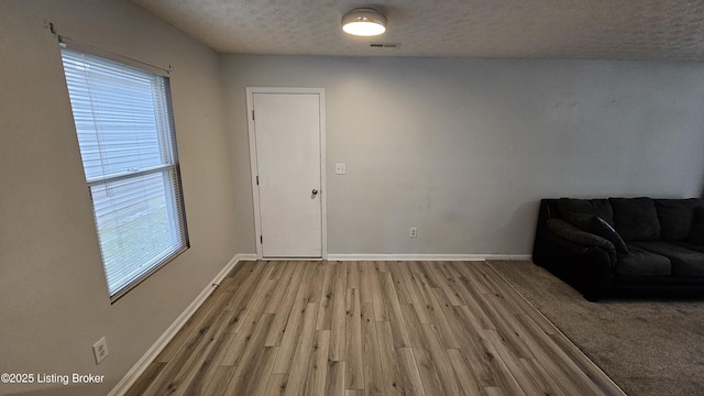 unfurnished living room with a textured ceiling, wood finished floors, visible vents, and baseboards