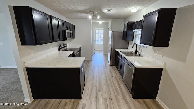 kitchen featuring a textured ceiling, dark cabinets, stainless steel appliances, a sink, and baseboards