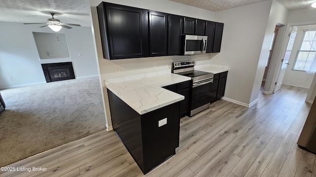 kitchen with a fireplace, appliances with stainless steel finishes, light wood-style floors, a textured ceiling, and dark cabinets