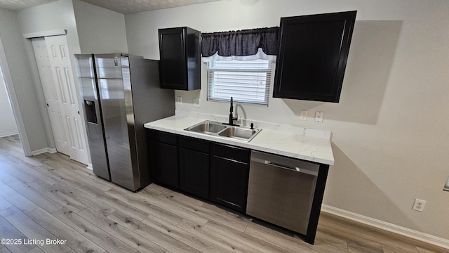 kitchen with appliances with stainless steel finishes, light wood-style floors, a sink, and dark cabinets