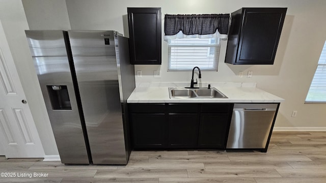 kitchen with light wood-style flooring, dark cabinetry, stainless steel appliances, and a sink