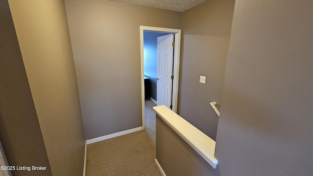 corridor featuring a textured ceiling, carpet flooring, an upstairs landing, and baseboards