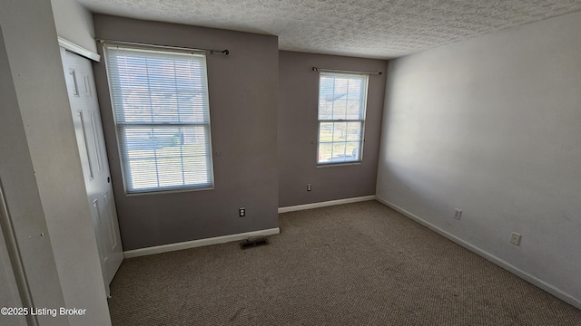 unfurnished room with a textured ceiling, carpet flooring, visible vents, and baseboards