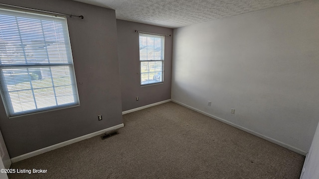 empty room featuring carpet floors, visible vents, a textured ceiling, and baseboards