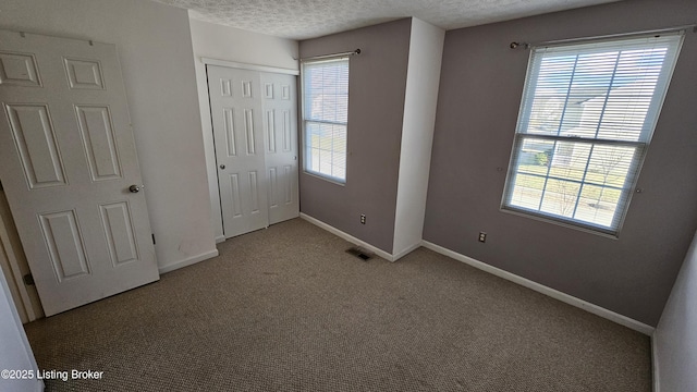 unfurnished bedroom with carpet, a closet, visible vents, a textured ceiling, and baseboards