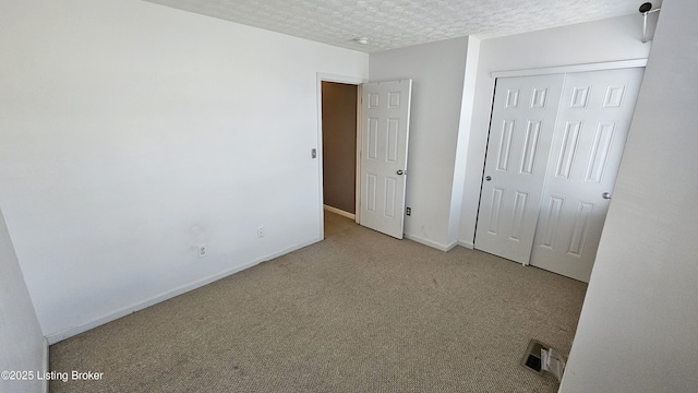 unfurnished bedroom featuring baseboards, visible vents, a textured ceiling, carpet flooring, and a closet