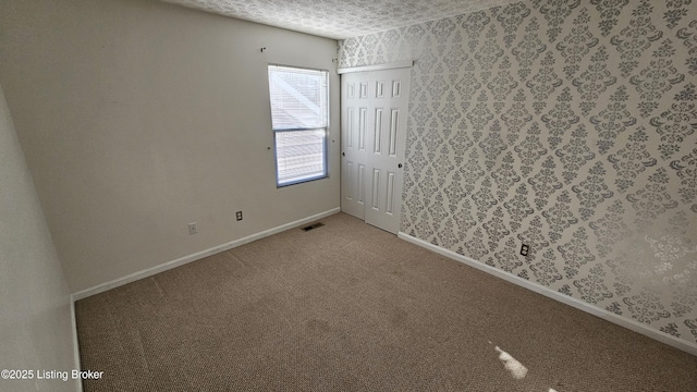 unfurnished room with wallpapered walls, visible vents, baseboards, a textured ceiling, and carpet floors