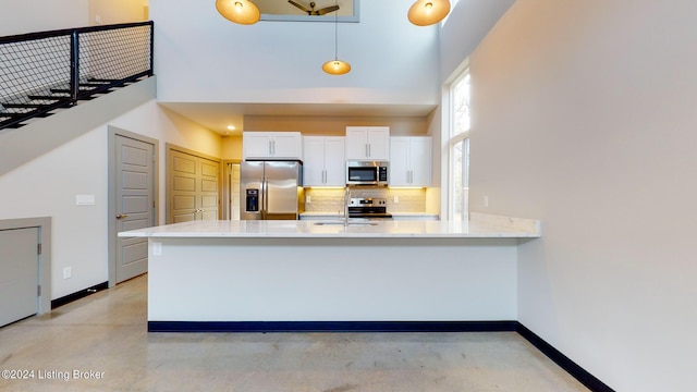 kitchen featuring stainless steel appliances, concrete flooring, a towering ceiling, and a peninsula