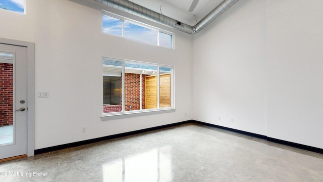 empty room featuring concrete flooring, a towering ceiling, and baseboards