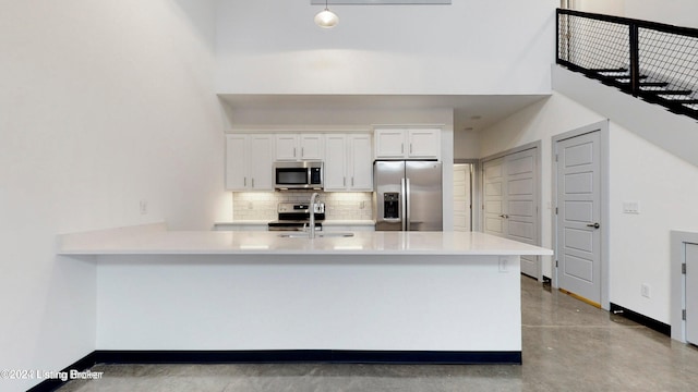 kitchen featuring a high ceiling, a sink, white cabinets, appliances with stainless steel finishes, and backsplash