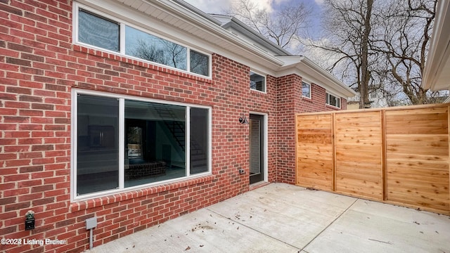 rear view of property featuring brick siding, a patio area, and fence