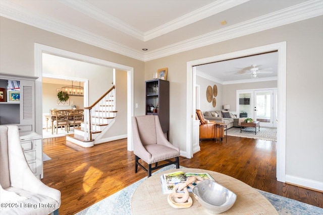 living area featuring crown molding, baseboards, wood finished floors, and ceiling fan with notable chandelier