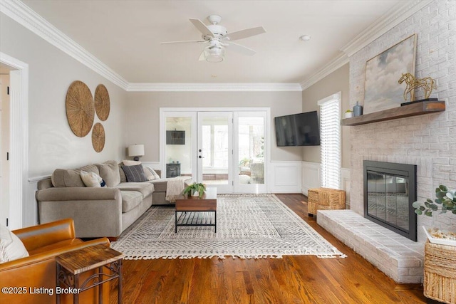 living area with a wainscoted wall, a fireplace, ornamental molding, and wood finished floors